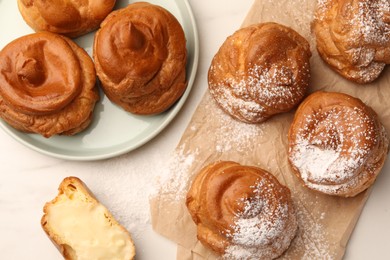 Photo of Delicious profiteroles with powdered sugar on white table, flat lay