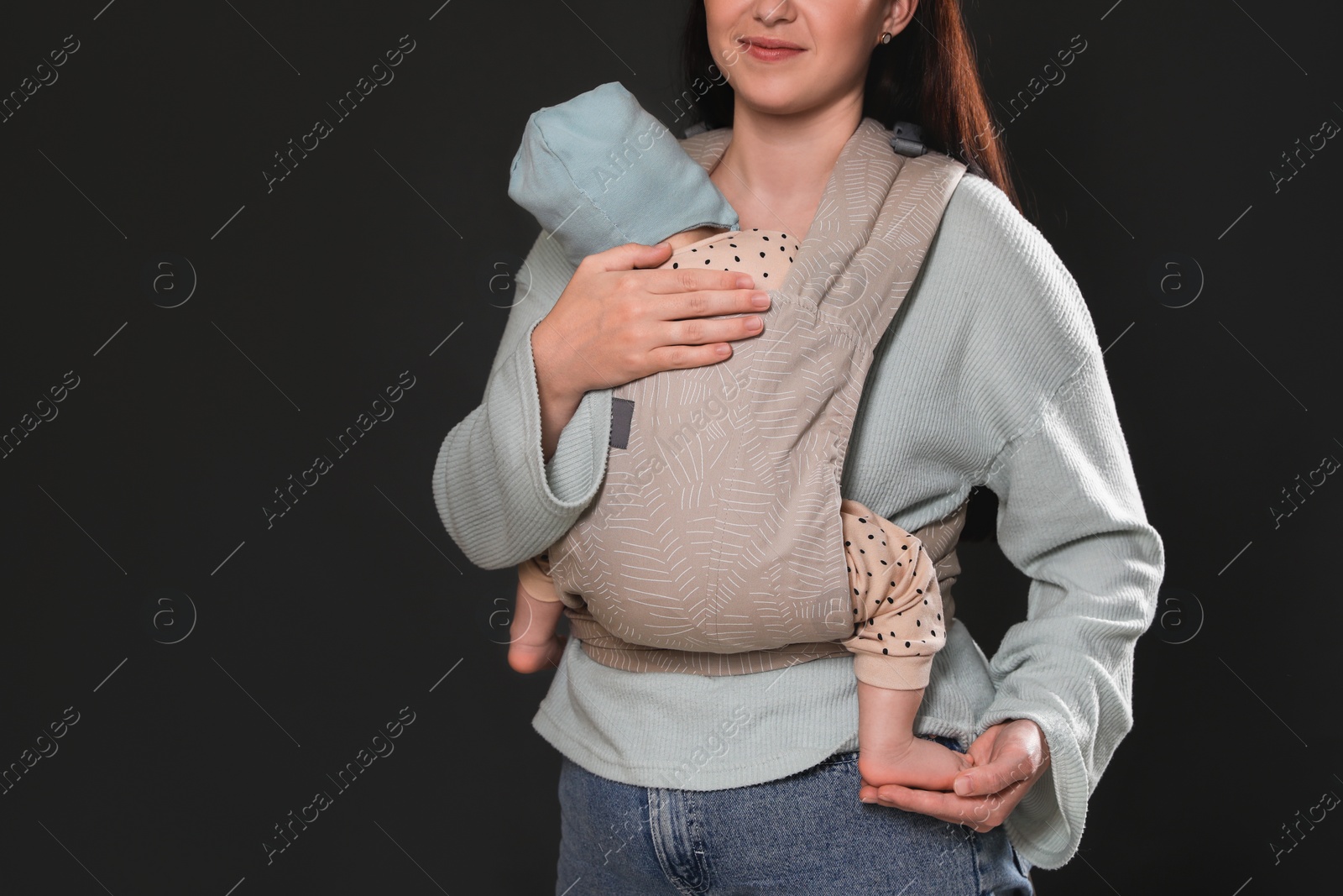 Photo of Mother holding her child in baby carrier on black background, closeup. Space for text