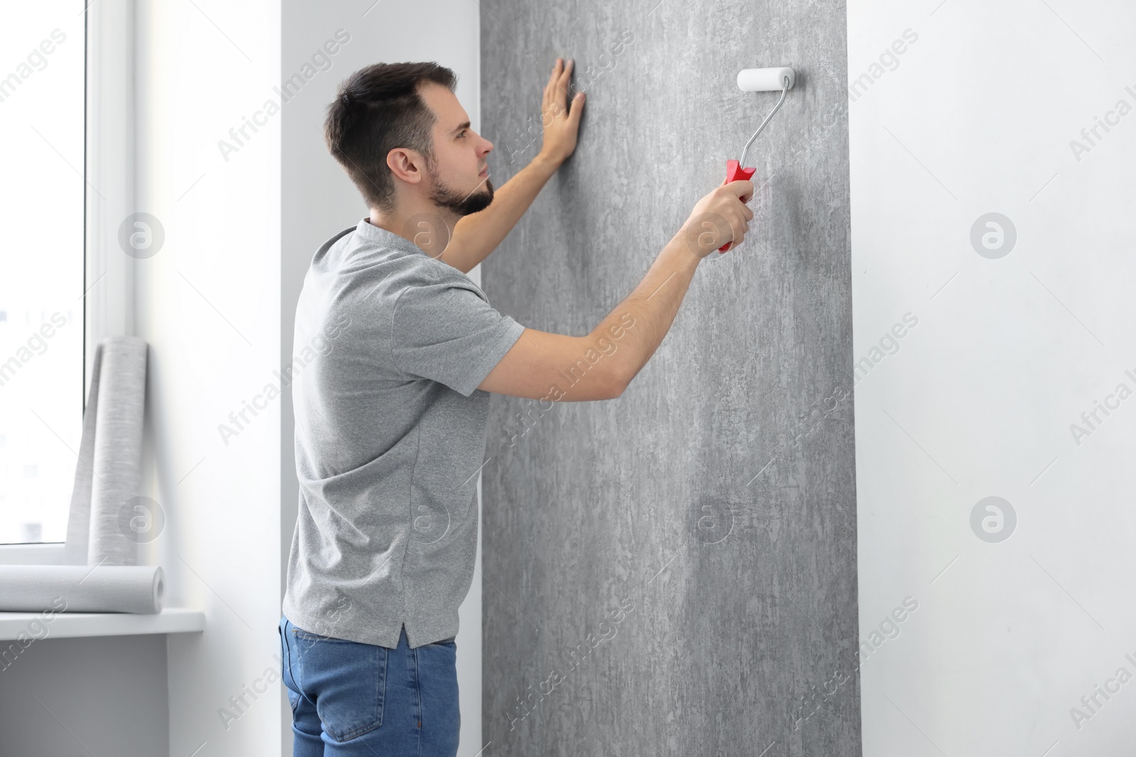 Photo of Man hanging stylish gray wallpaper in room