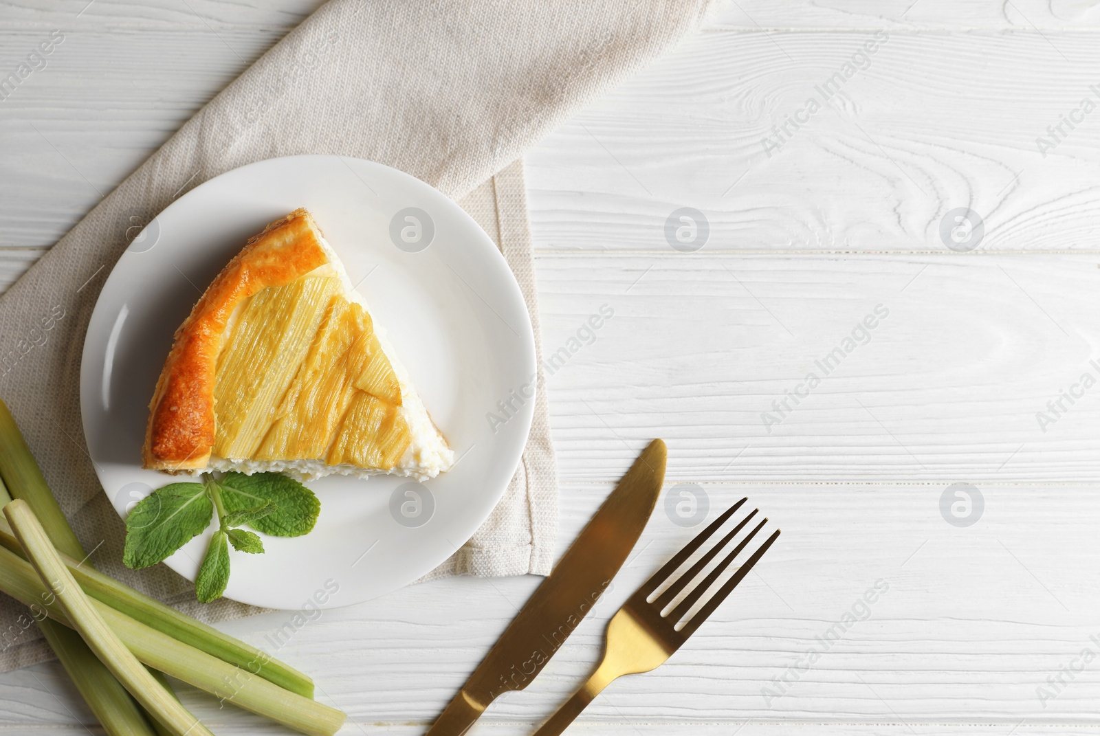 Photo of Piece of freshly baked rhubarb pie, stalks and cutlery on white wooden table, flat lay. Space for text