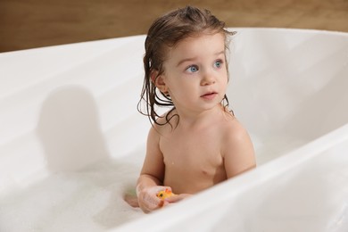 Photo of Cute little girl washing hair with shampoo in bathroom