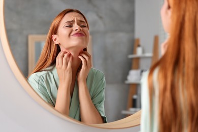 Photo of Suffering from allergy. Young woman scratching her neck near mirror in bathroom