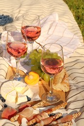 Photo of Glasses of delicious rose wine and food on white picnic blanket outdoors