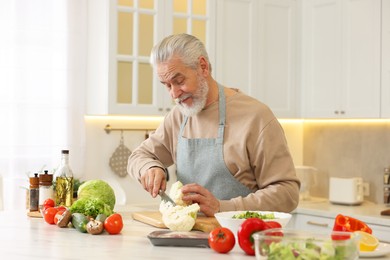 Photo of Happy man cutting cauliflower at table in kitchen