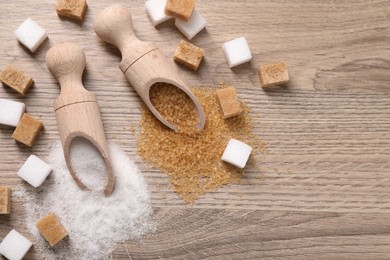 Photo of Scoops with different types of sugar on wooden table, flat lay. Space for text