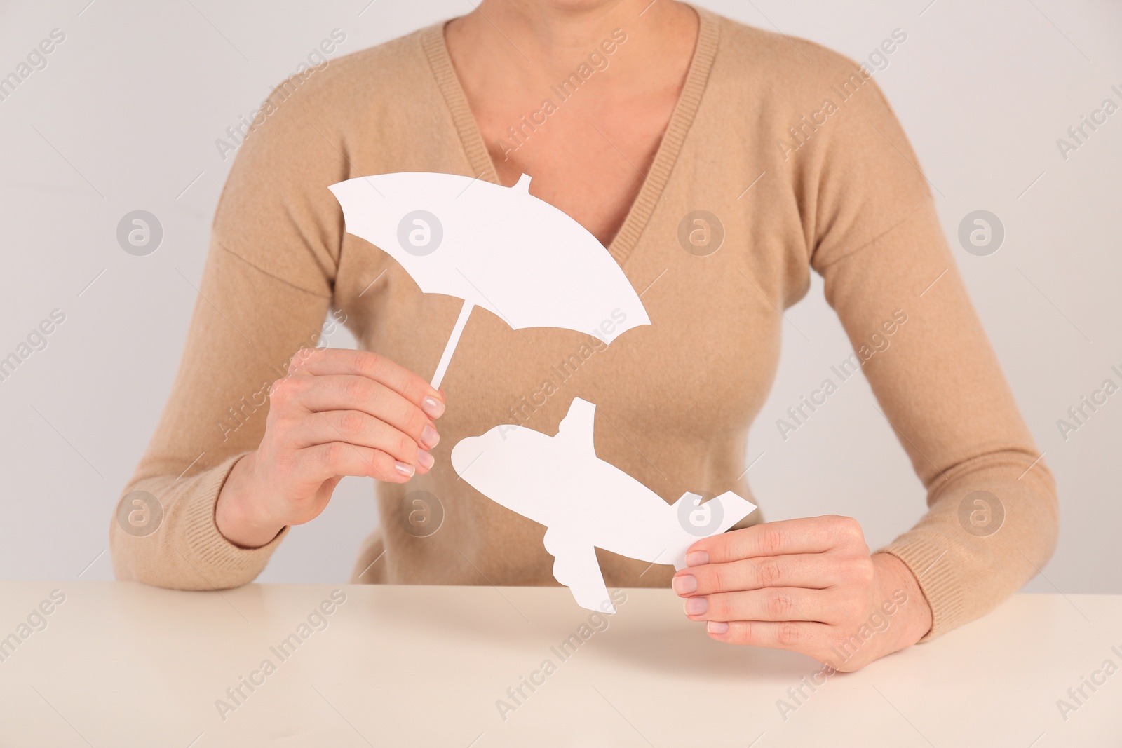 Photo of Insurance agent covering paper plane with umbrella cutout at table, closeup. Travel safety concept