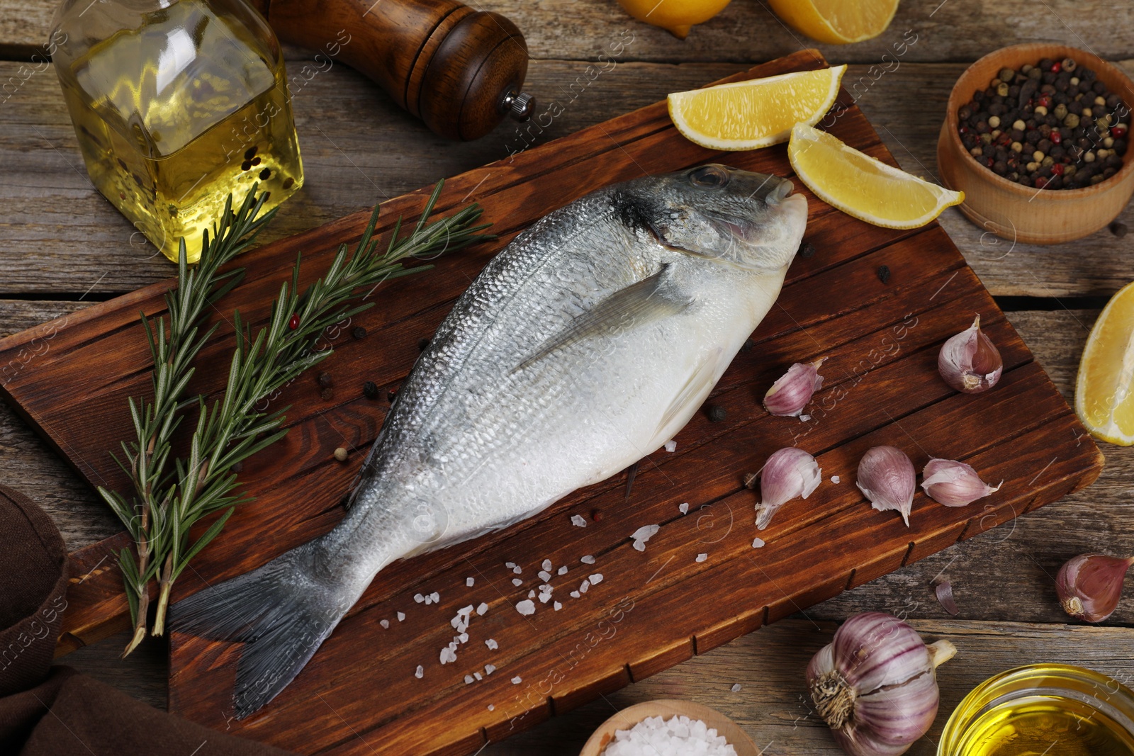 Photo of Raw dorado fish, lemon wedges and spices on wooden table