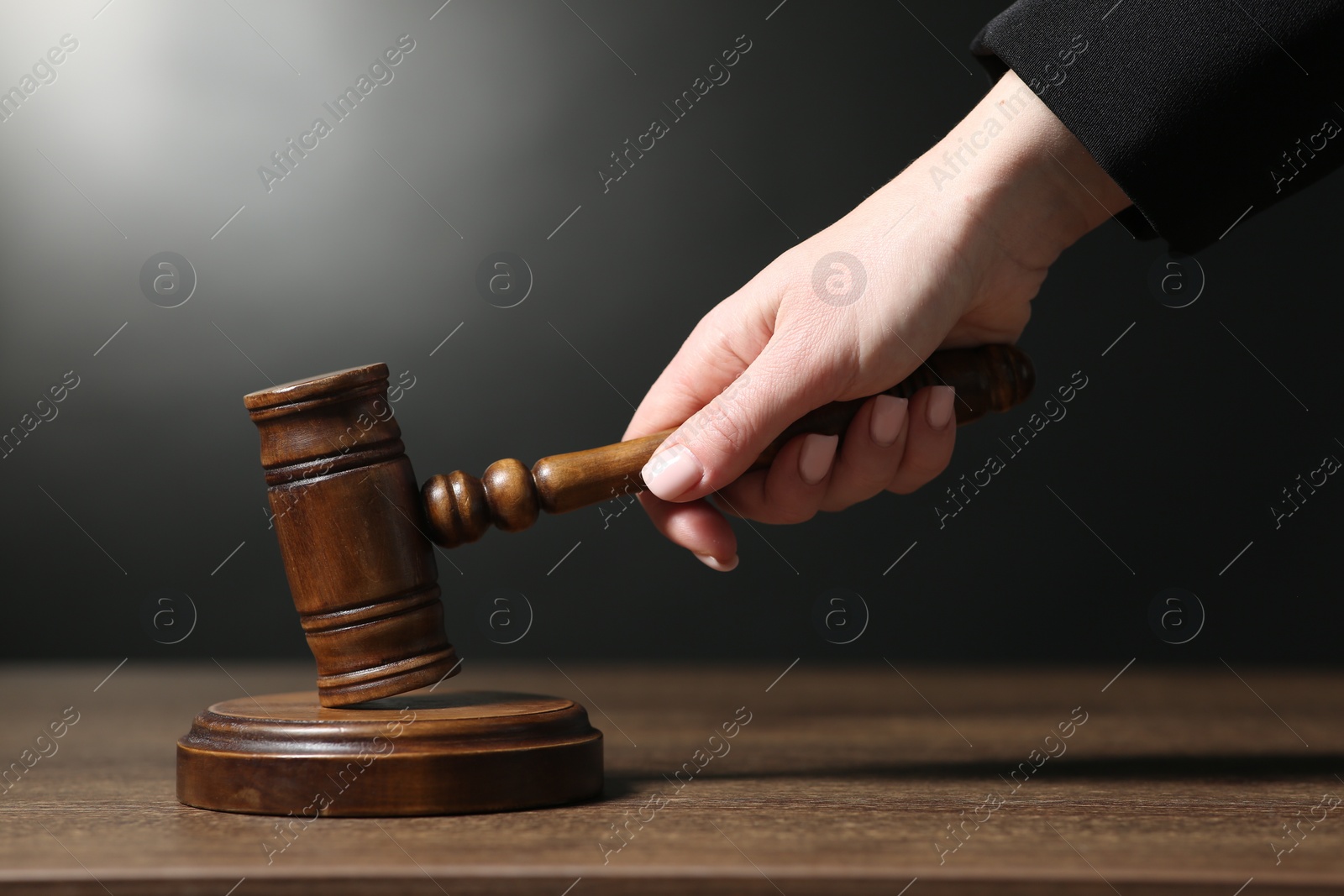 Photo of Judge striking mallet at wooden table against dark background, closeup