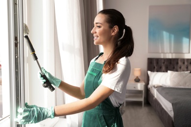 Photo of Professional janitor cleaning window with mop in bedroom