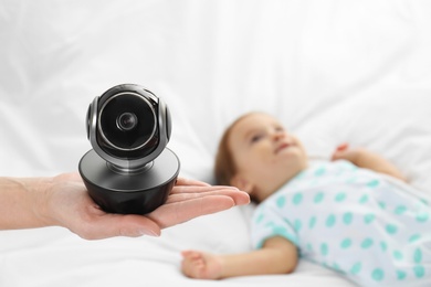 Photo of Woman holding baby camera near child on bed. Video nanny