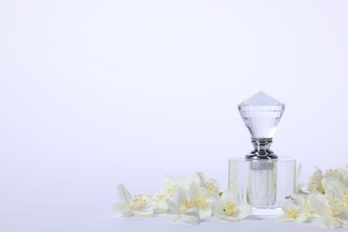 Photo of Aromatic perfume in bottle and beautiful jasmine flowers on white background, space for text