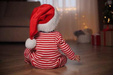 Baby in Christmas pajamas and Santa hat indoors, back view