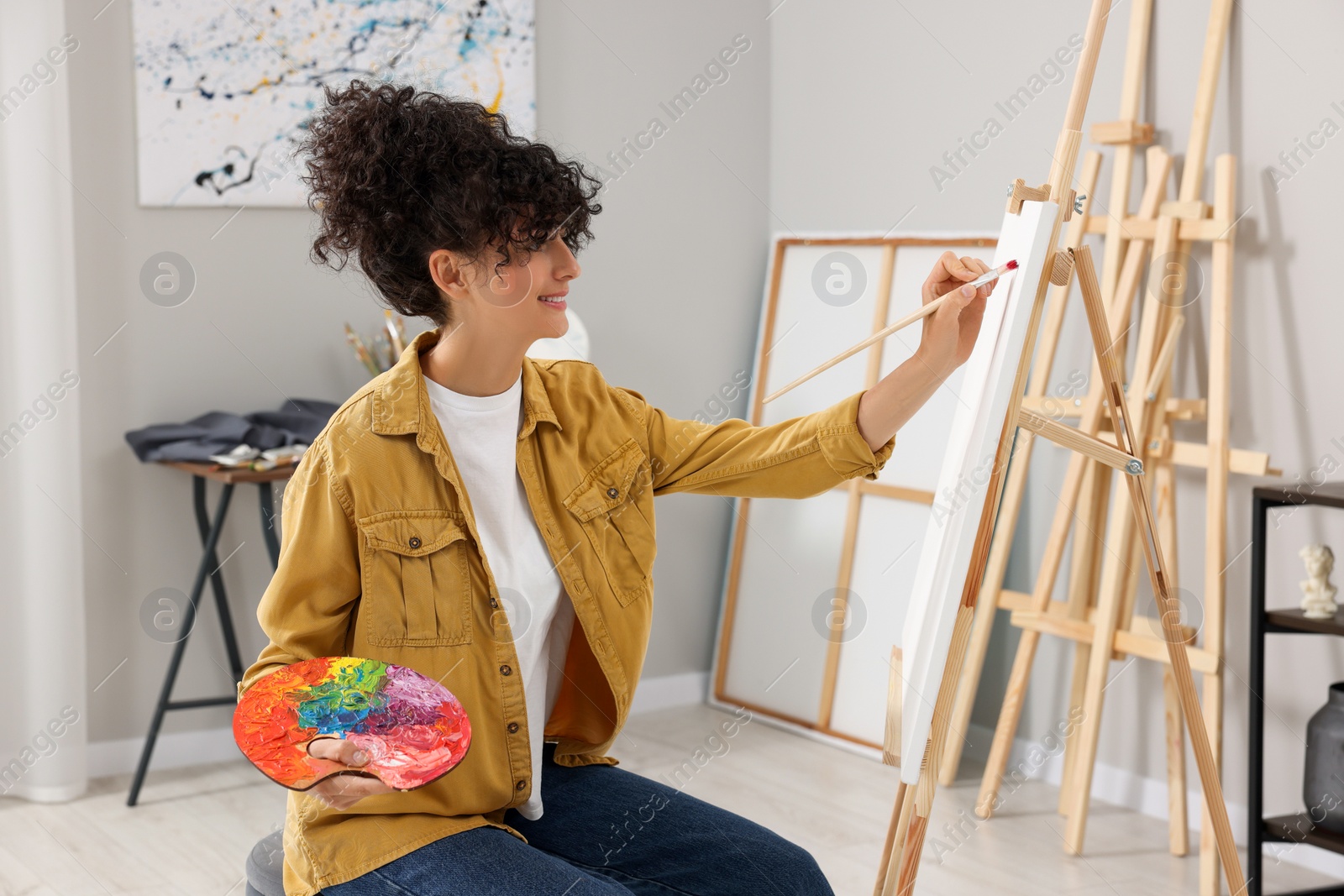 Photo of Young woman painting on easel with canvas in studio