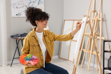 Photo of Young woman painting on easel with canvas in studio