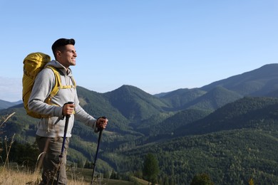 Tourist with backpack and trekking poles hiking through mountains, space for text