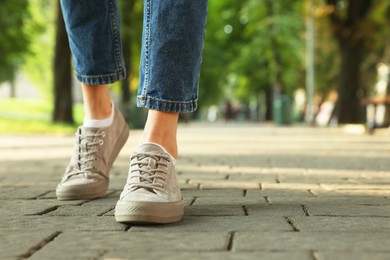 Photo of Woman in stylish sneakers walking on city street, closeup. Space for text