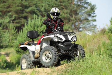 Man driving modern quad bike on sandy road near forest. Extreme sport