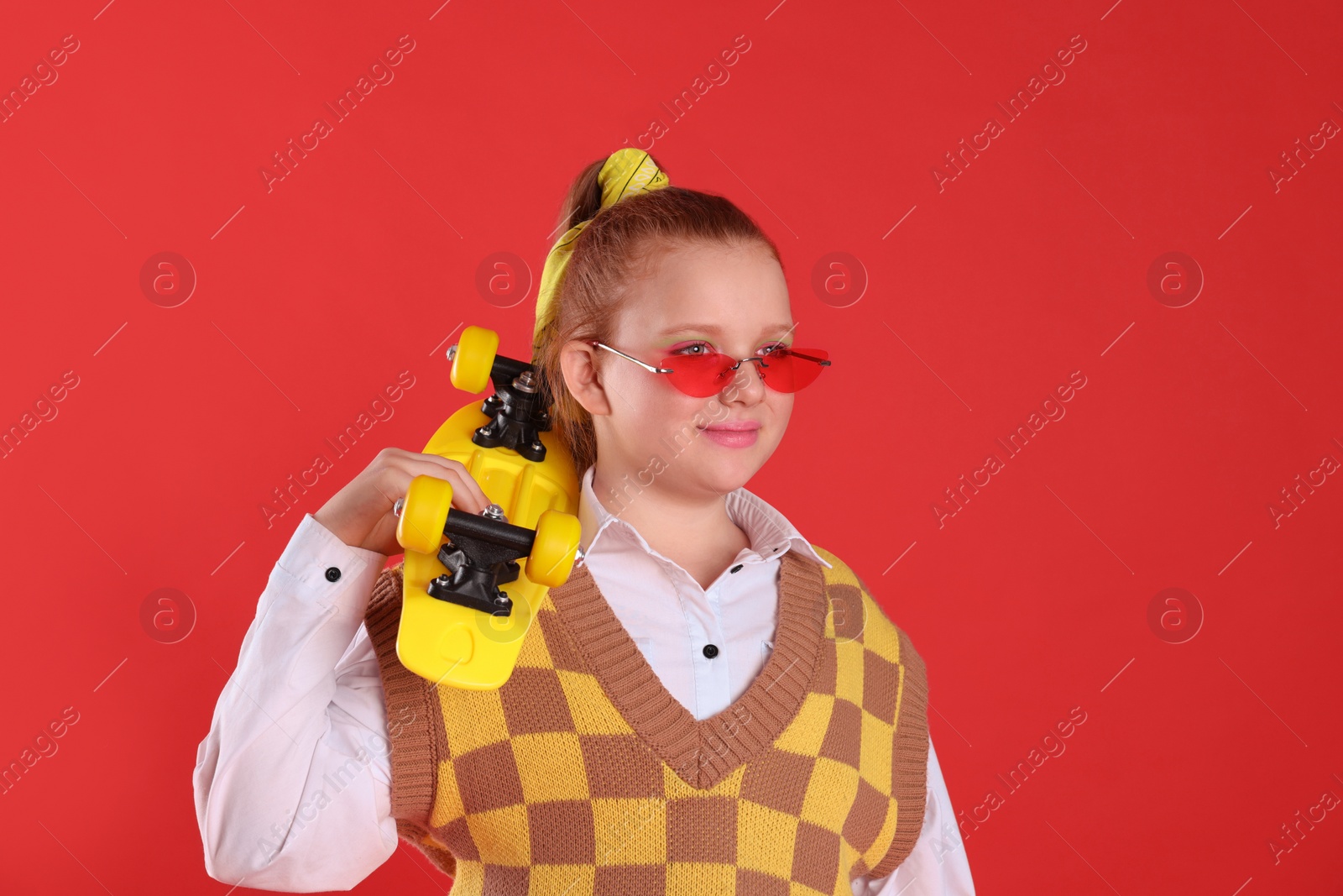 Photo of Cute indie girl with sunglasses and penny board on red background