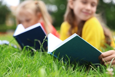 Photo of Little children reading books on green grass, closeup