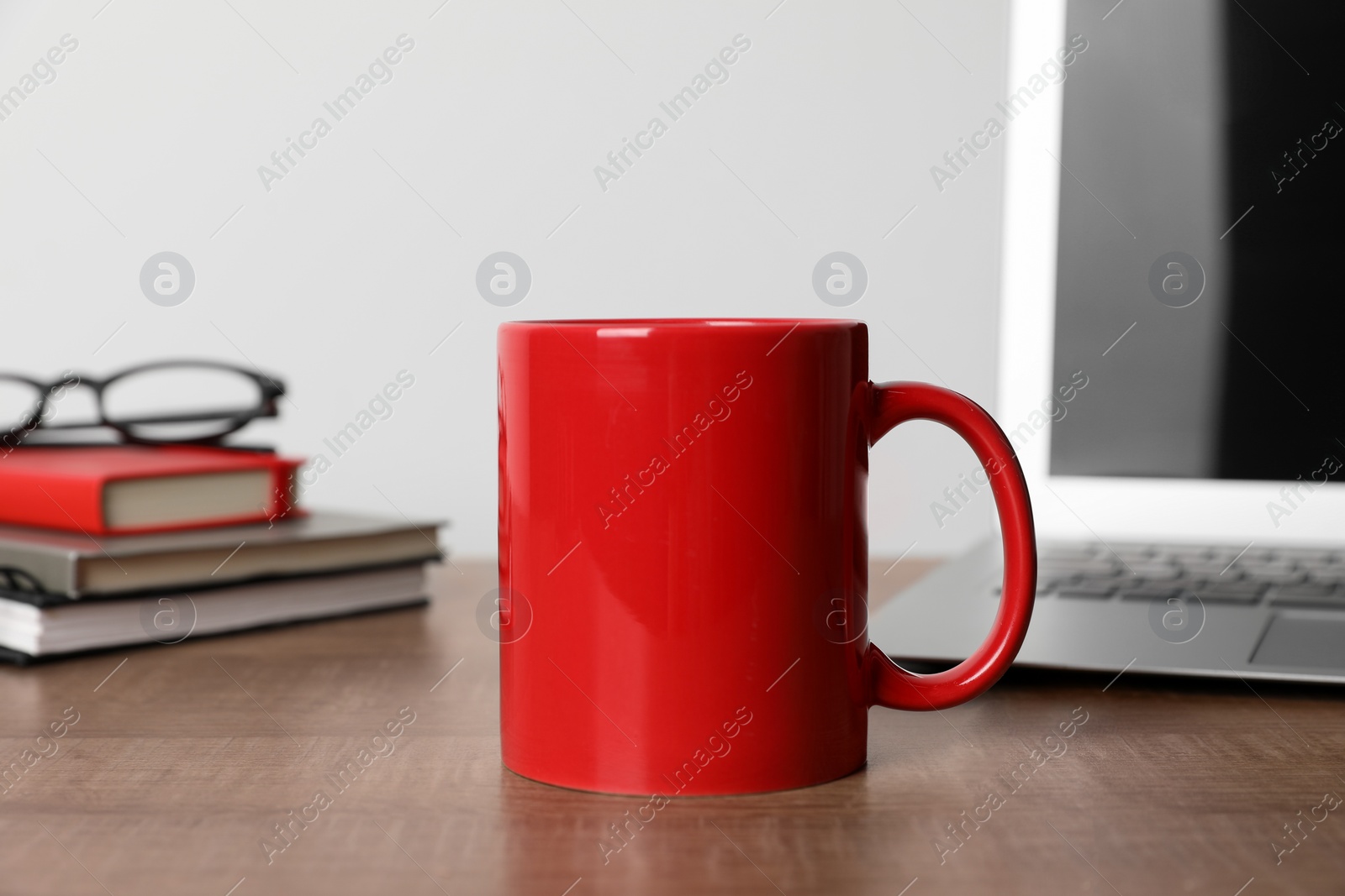 Red ceramic mug, stationery, glasses and laptop on wooden table at workspace Photo of Red ceramic mug, stationery, glasses and laptop on wooden table at workspace