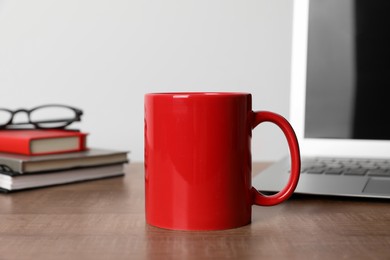 Photo of Red ceramic mug, stationery, glasses and laptop on wooden table at workspace