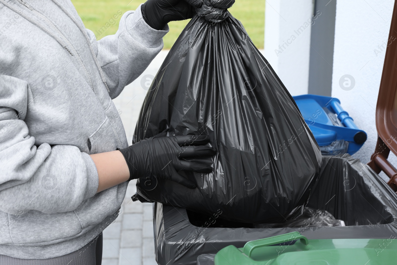 Photo of Woman throwing trash bag full of garbage in bin outdoors, closeup. Recycling concept