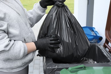 Photo of Woman throwing trash bag full of garbage in bin outdoors, closeup. Recycling concept