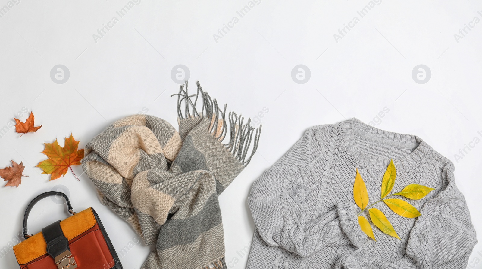 Photo of Stylish outfit and autumn leaves on white background, top view with space for text. Trendy warm clothes