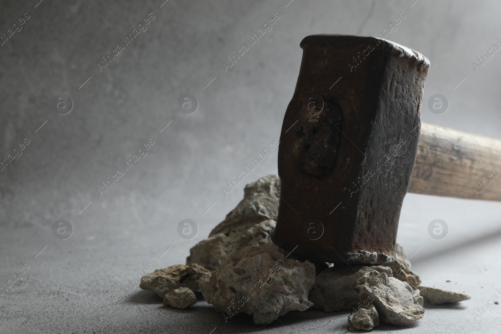 Photo of One sledgehammer and pieces of broken stones on grey background, closeup. Space for text