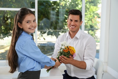 Schoolgirl congratulating her pedagogue with bouquet in classroom. Teacher's day