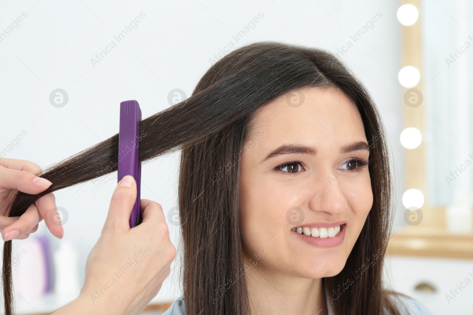 Photo of Hairdresser using modern flat iron to style client's hair in salon