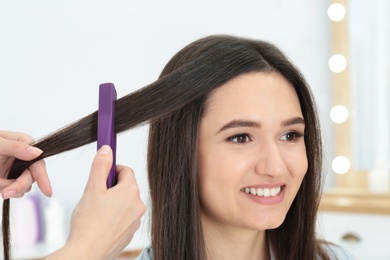 Hairdresser using modern flat iron to style client's hair in salon