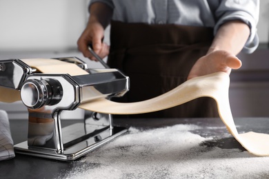 Photo of Young man preparing noodles on pasta maker at table