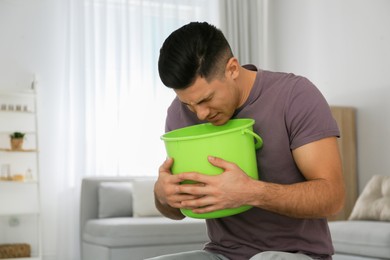 Photo of Man with bucket suffering from nausea at home, space for text. Food poisoning
