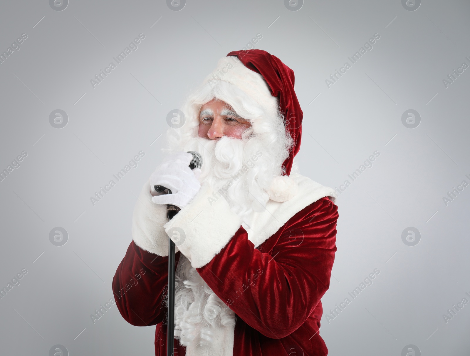 Photo of Santa Claus singing with microphone on light grey background. Christmas music