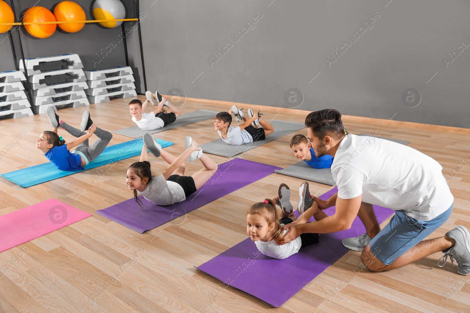 Photo of Trainer helping children to do physical exercise in school gym. Healthy lifestyle