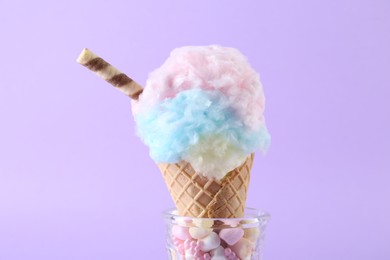 Photo of Sweet cotton candy in waffle cone on purple background, closeup