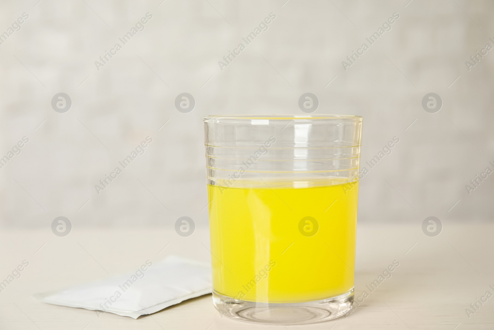 Photo of Glass of dissolved medicine and sachet on white wooden table