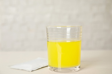 Glass of dissolved medicine and sachet on white wooden table