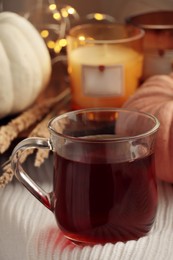 Photo of Cup of hot drink, candles and pumpkins on white knitted blanket indoors