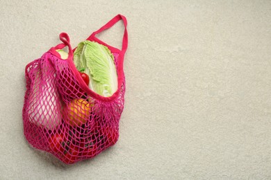 Photo of Fresh Chinese cabbage and other products in string bag on light textured table, top view. Space for text