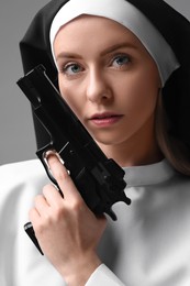 Woman in nun habit holding handgun on grey background, closeup