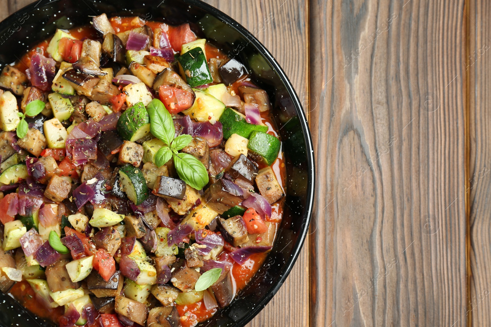 Photo of Delicious ratatouille in baking dish on wooden table, top view. Space for text