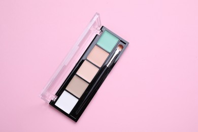 Photo of Colorful contouring palette with brush on pale pink background, top view. Professional cosmetic product