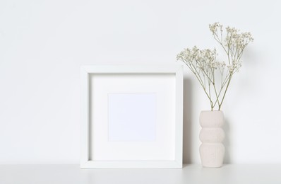Photo of Empty photo frame and vase with dry decorative gypsophila flowers on white table. Mockup for design