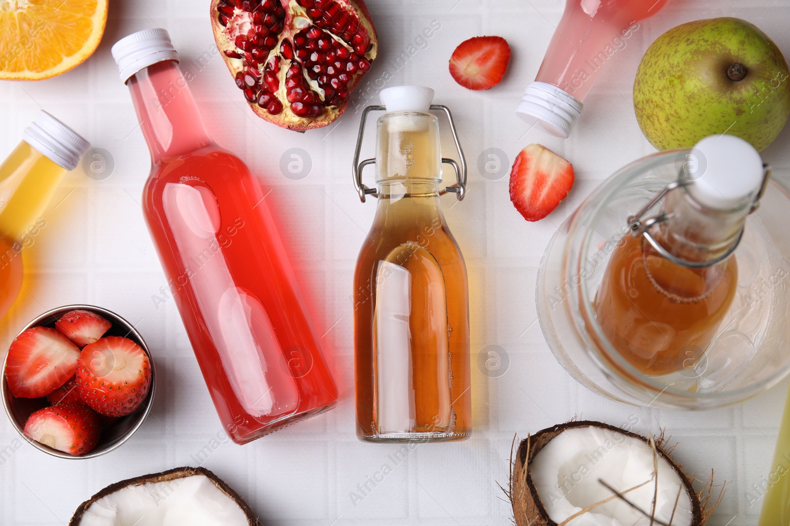 Photo of Tasty kombucha in glass bottles and fresh fruits on white tiled table, flat lay