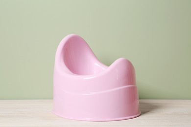 Photo of Pink baby potty on white wooden table against olive background. Toilet training