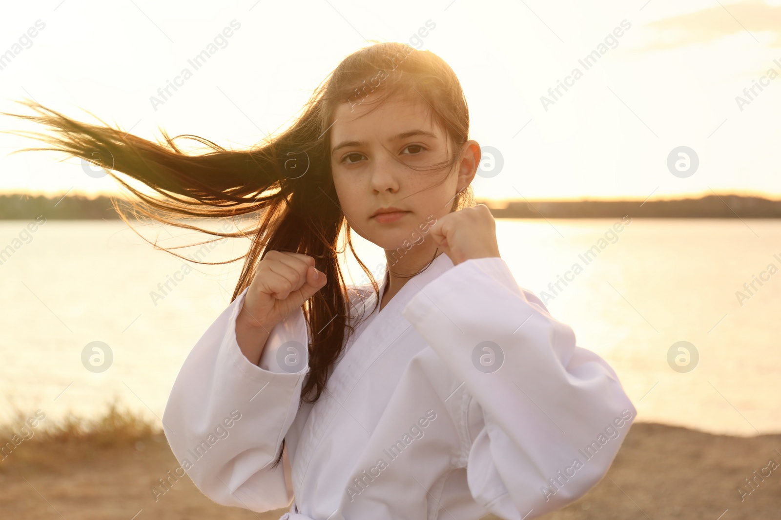 Photo of Cute little girl in kimono practicing karate near river at sunset