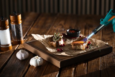 Cooking meat medallions with manual gas burner on wooden table in photo studio. Food stylist