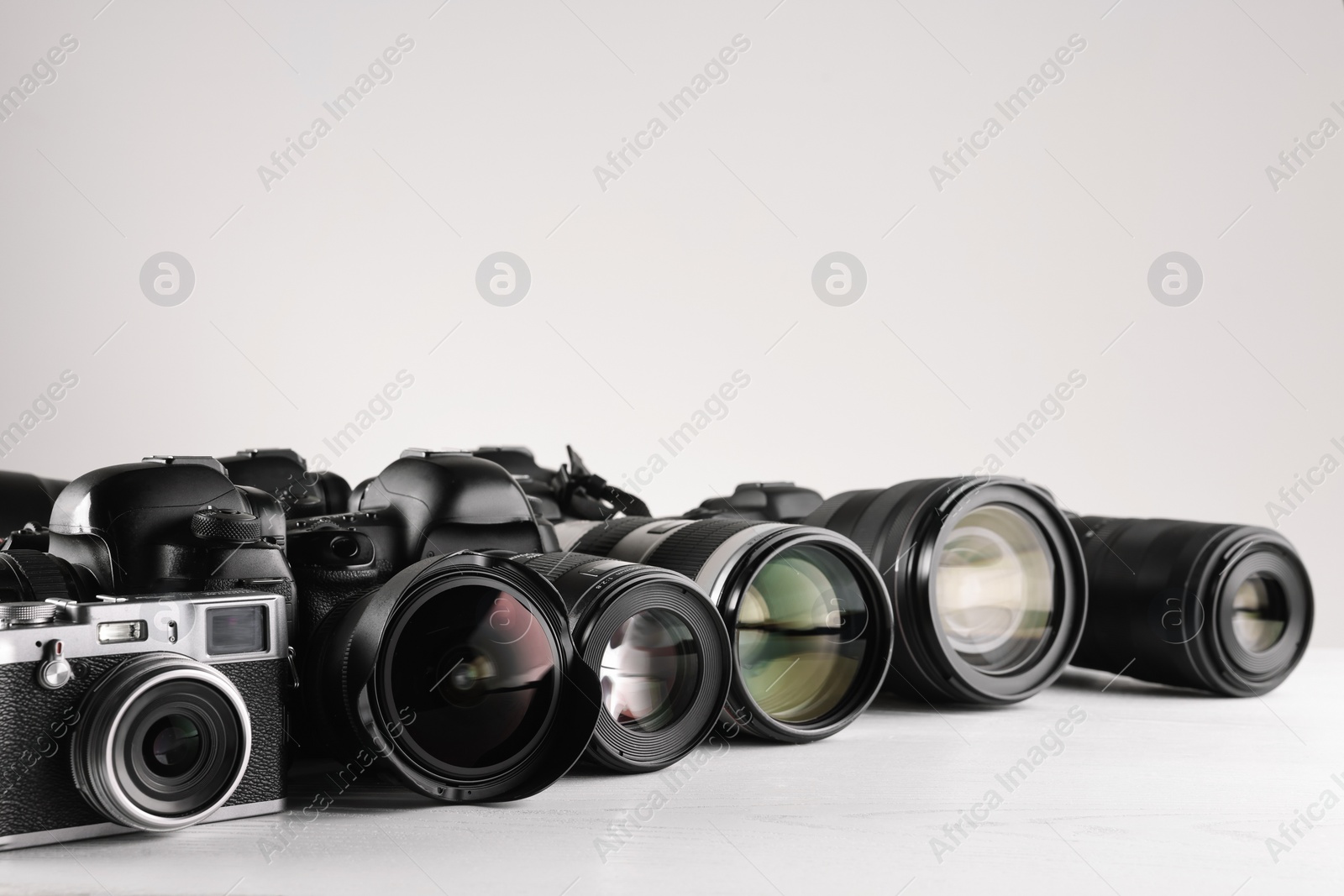 Photo of Modern cameras on white wooden table, space for text